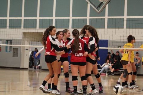 The Varsity Volleyball team comes together in a huddle.